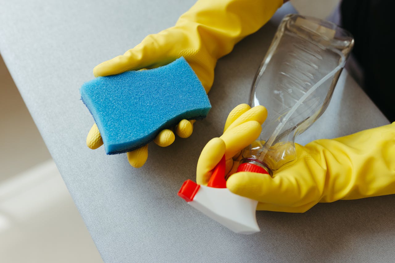gallery-04 Close-up of hands in gloves holding a sponge and spray bottle for cleaning.